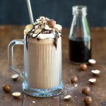 Chocolate milkshake in a tall glass with whipped cream, chocolate sauce and chocolate covered malt balls.
