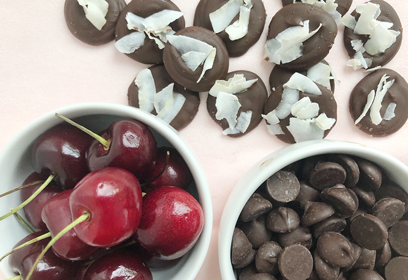 Bowl of cherries next to a bowl of chocolate chips and chocolate pieces with coconut shavings.