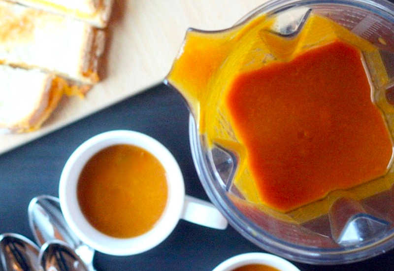 Tomato soup in a blender next to a bowl of tomato soup.