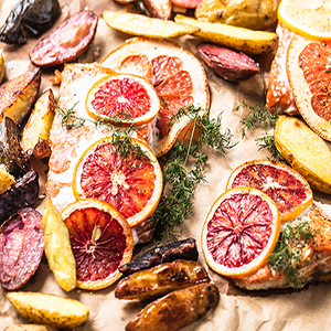 Citrus roasted salmon topped with sliced oranges, surrounded by roasted potatoes slices.