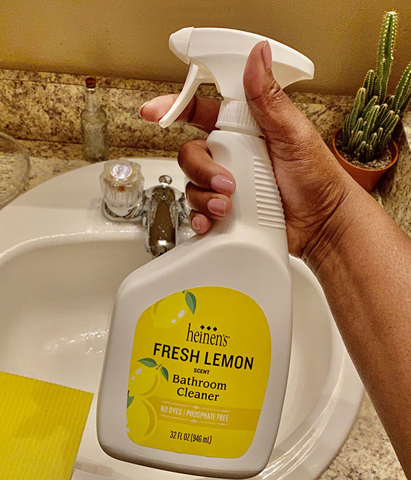 Hand holding Heinen's fresh lemon scented bathroom cleaner in front of a bathroom sink.