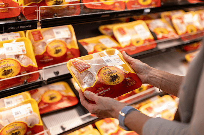 Customer Hands Holding a Package of Gerber's Care Certified Chicken in front of the Gerber Chicken Product Display