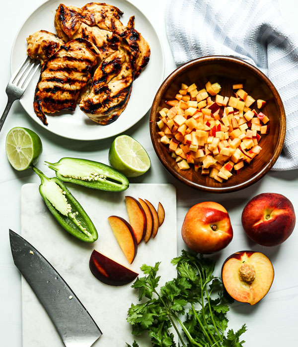 Plate of grilled chicken next to stone fruit, jalapeños, lime and cilantro.