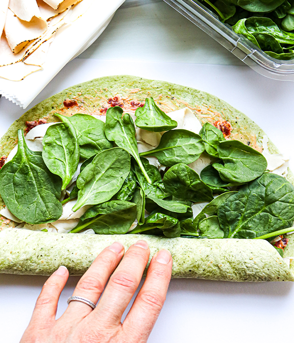 Wrap with turkey, sundried tomatoes, and spinach being rolled.