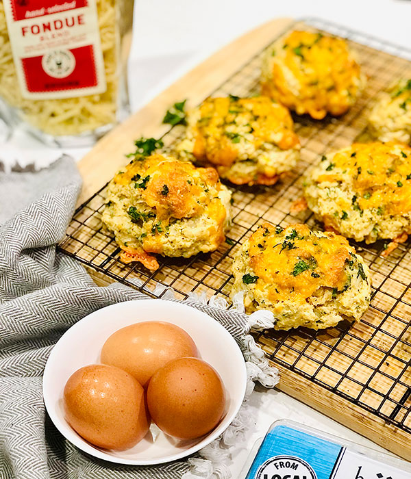 Tray with cheddar baked biscuits topped with cheese and parsley next to a small bowl with eggs.