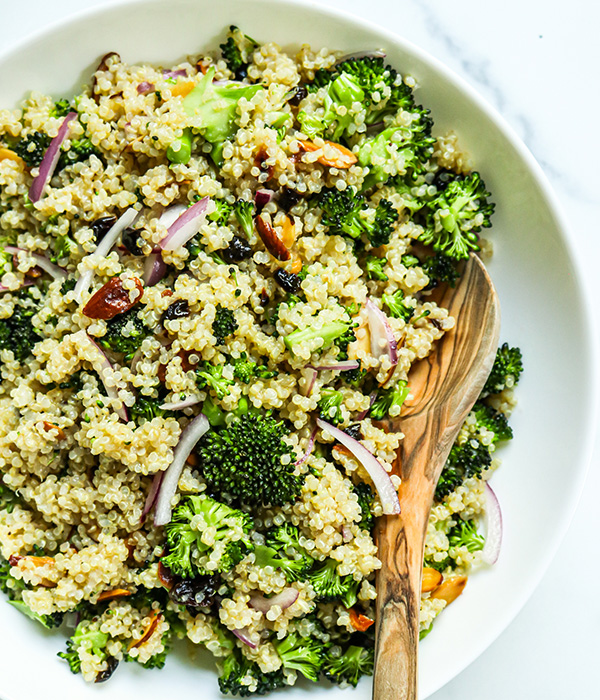 Quinoa salad with broccoli and red onion in a serving bowl with a wooden serving spoon. 