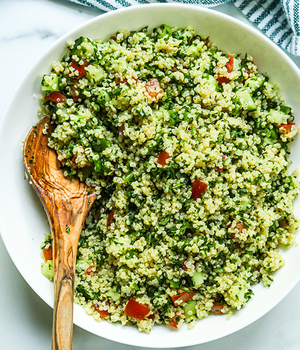 Quinoa salad with tomatoes, cucumber and parsley served in a bowl with a wooden serving spoon. 