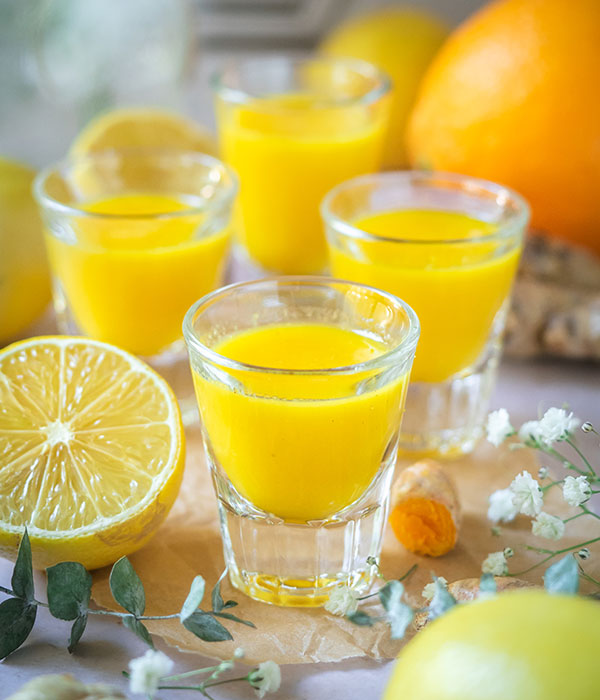 Yellow immunity shots served in shot glasses next to oranges, lemons and ginger.