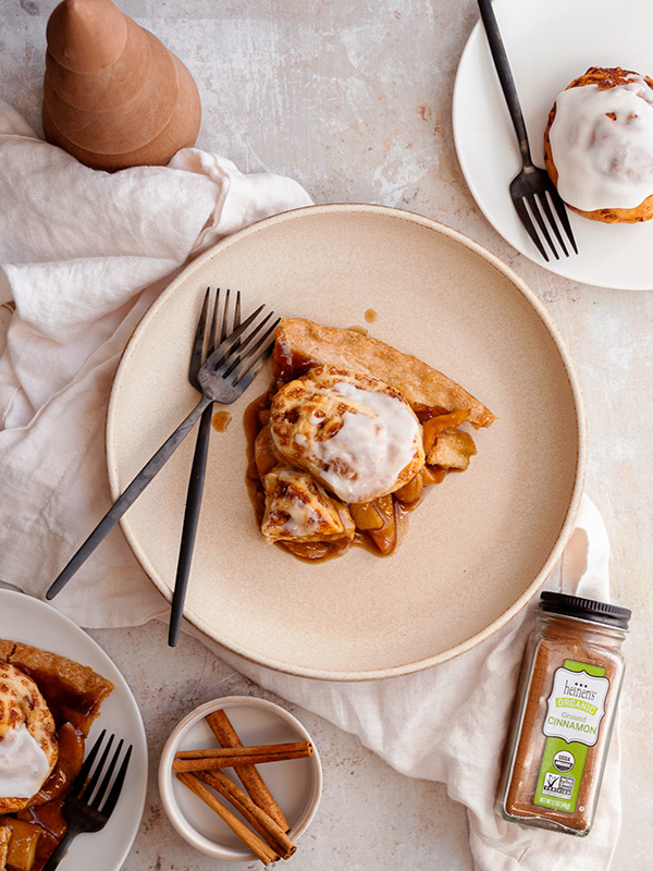 Cinnamon Roll Apple Pie on a plate next to fresh cinnamon sticks and Heinen's organic cinnamon.