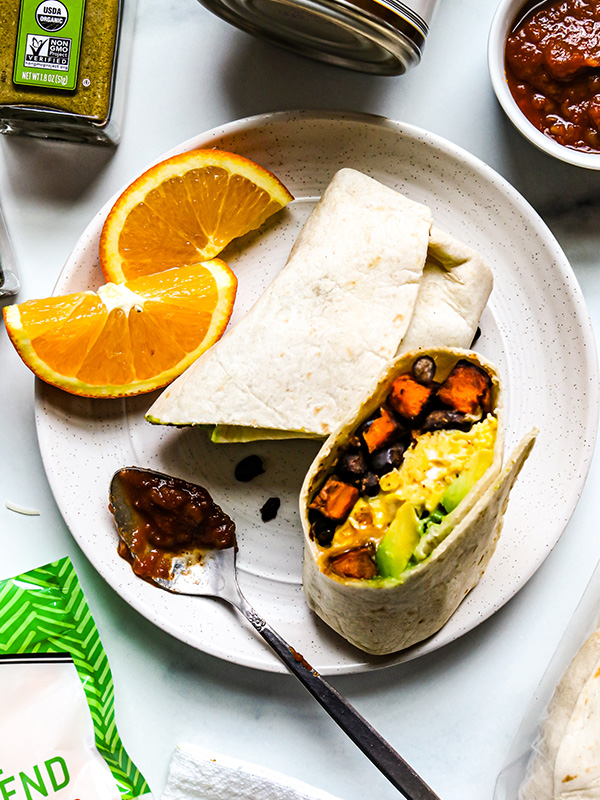 Sweet potato and black bean burrito with egg and avocado on a plate with oranges.