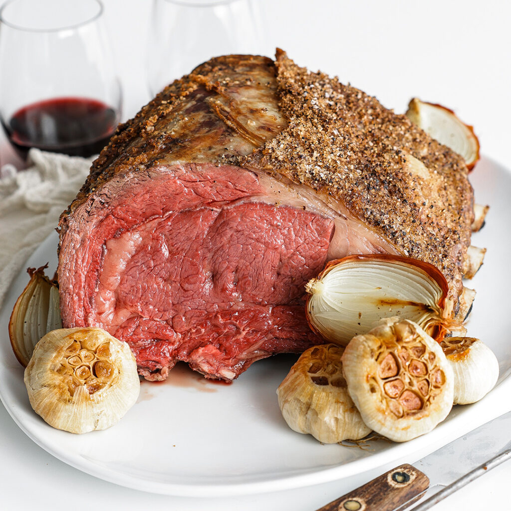 Medium-rare rib roast on a plate with onions and fresh garlic.