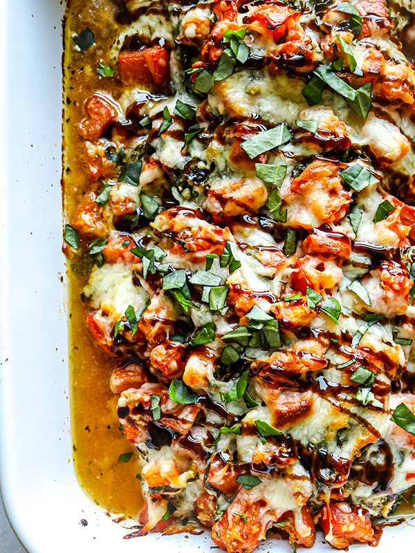 Baking dish with chicken topped with mozzarella cheese, tomatoes and basil.