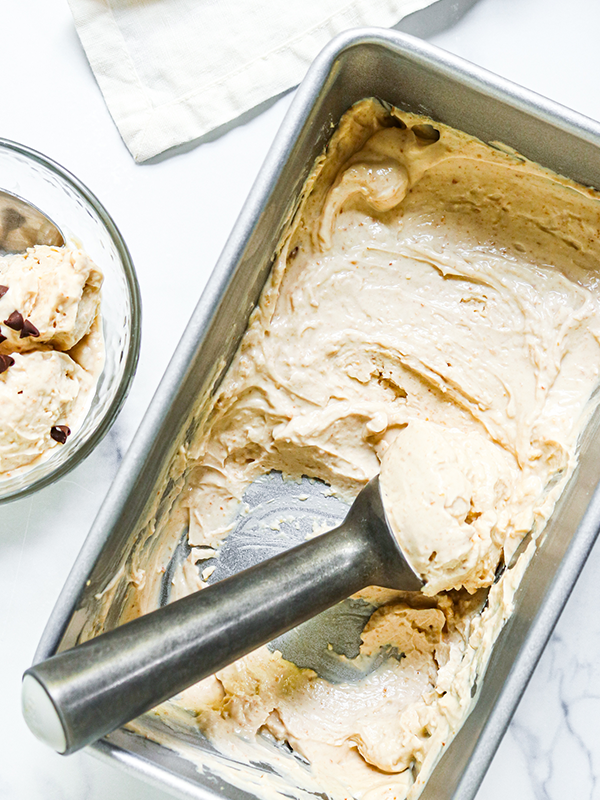 Greek yogurt ice cream in a metal loaf pan with an ice cream scoop.