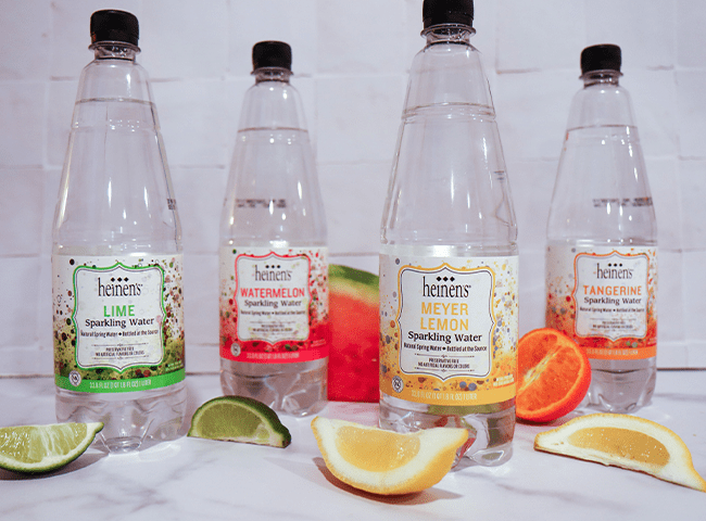 4 flavors of heinen's sparkling water with some fruit on the side