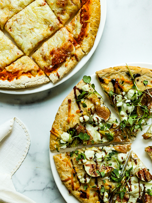 Two sliced flatbread pizzas, one plain cheese and one with figs, goat cheese, arugula, and balsamic drizzle.