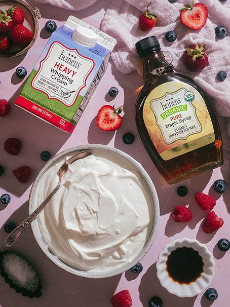 Whipped yogurt in a bowl next to a container of heavy whipping cream and pure maple syrup.