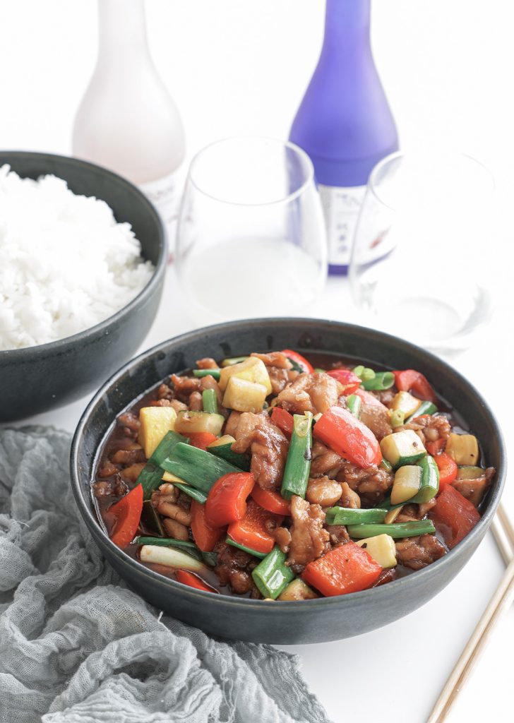 Bowl of with Hunan chicken, red bell peppers, yellow squash, zucchini, and green onions beside a bowl of white rice.
