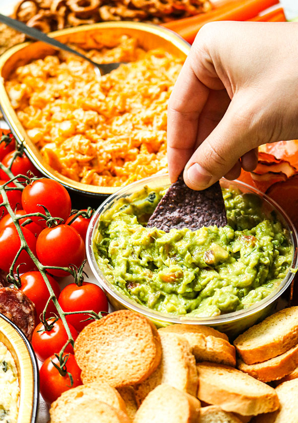 A Hand Dipping a Blue Tortilla Chip into Heinen's Fresh Guacamole