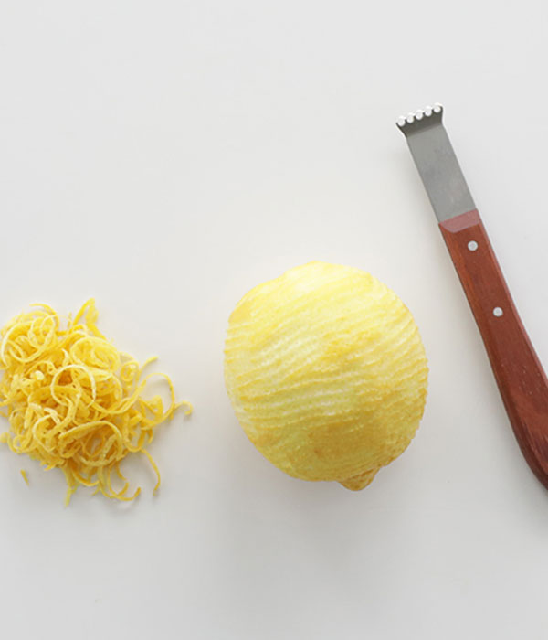 A whole peeled lemon with lemon zest and a lemon peeler beside the lemon