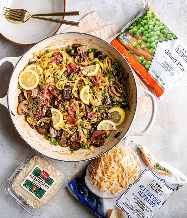 Spring Vegetable Fettuccine Alfredo in a dish with Frozen Fettuccine Alfredo Packaging, Heinen's Parmigiano Reggiano Packaging and Frozen Pea Packaging