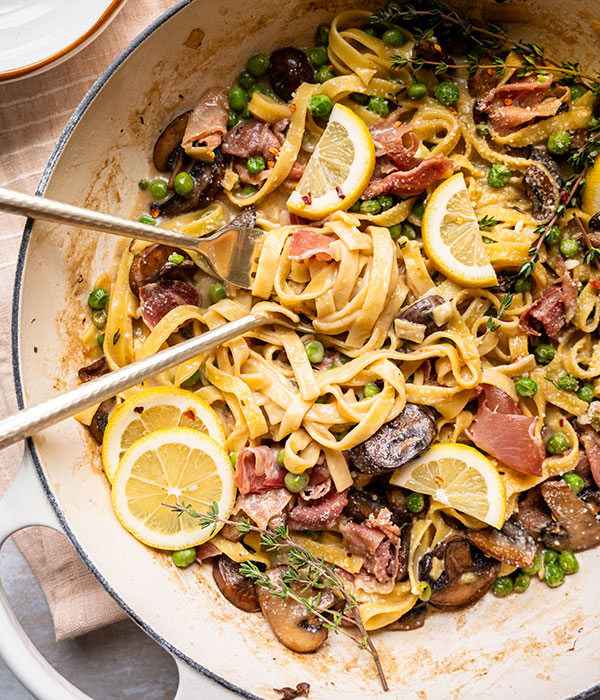 Spring Vegetable Fettuccine Alfredo in a Dish with Lemon Slices and Serving Utensils