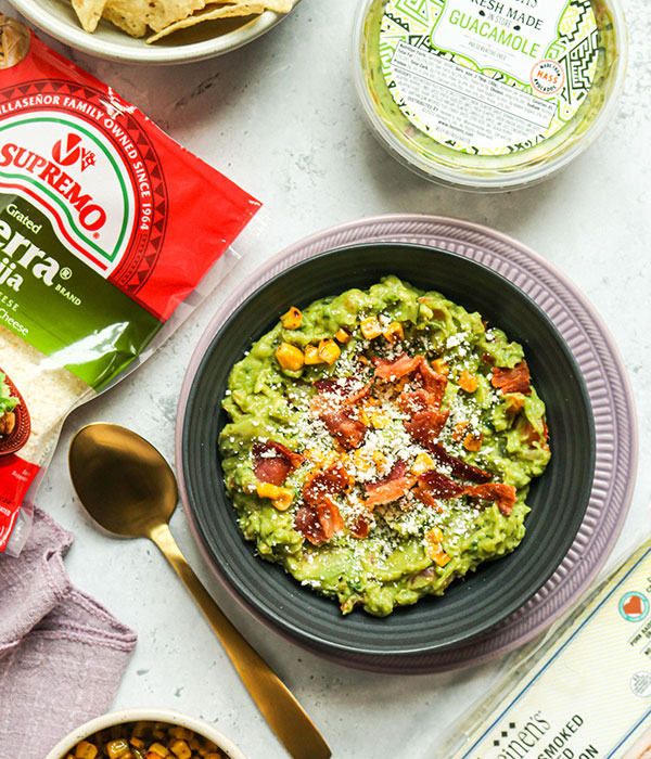 A Bowl of Guacamole with Roasted corn, Cooked Bacon and Fresh Cotija Cheese On Top