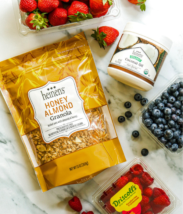 Heinen's Honey Almond Granola, Heinen's Organic Coconut Oil, Strawberries, and Blueberries on white marble table.