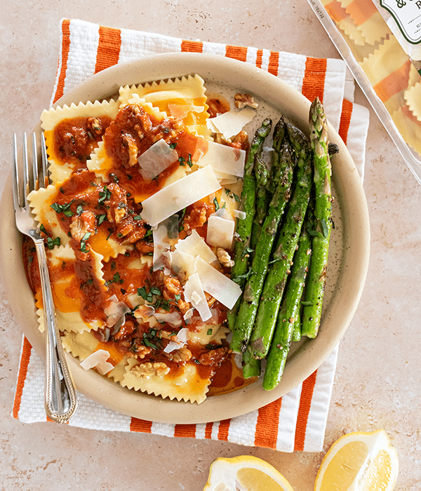 A Bowl of Asparagus and Gruyere Ravioli on an Orange Striped Napkin with a Tomato Butter Sauce and Parmesan Cheese