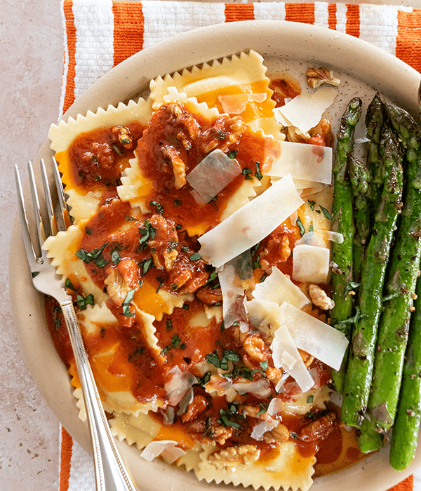 A Bowl of Asparagus and Gruyere Ravioli on an Orange Striped Napkin with a Tomato Butter Sauce and Parmesan Cheese