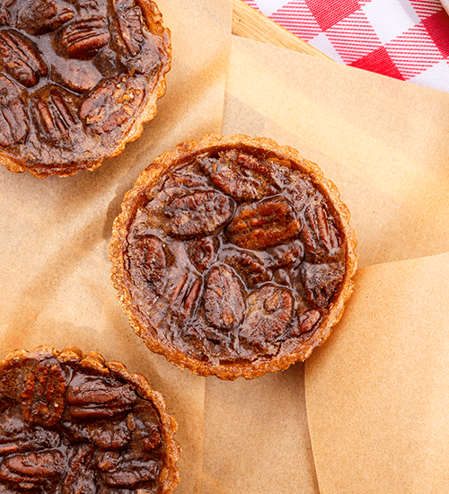 Three Heinen's Pecan Bourbon Tarts on Butcher Paper and a Red and White Checkered Blanket