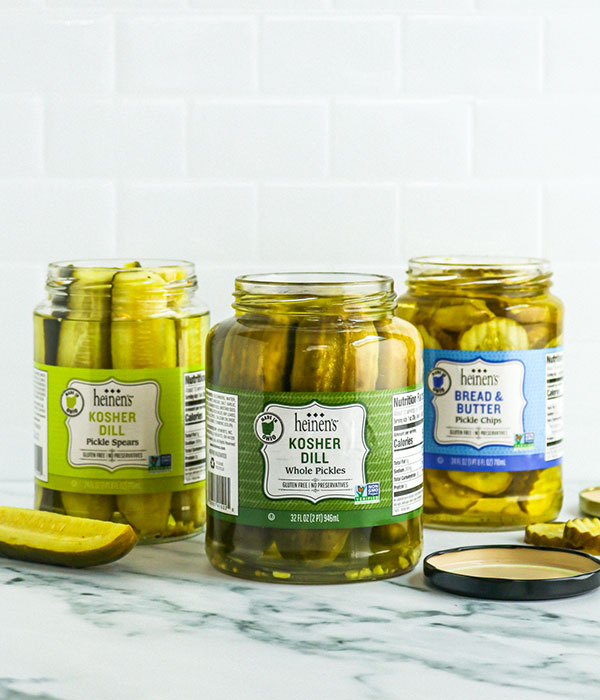 Three Open Jars of Heinen's Deli Pickles with Pickle Chips and Spears Sitting Beside the Jars