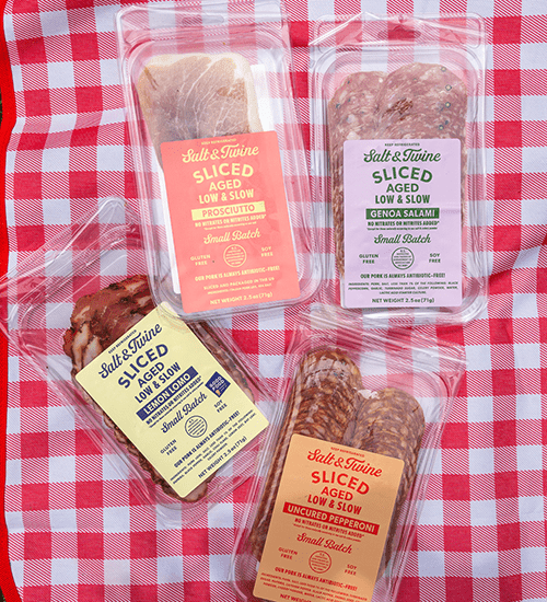 Four Packages of Salt & Twine Charcuterie Meats on a Red and White Checkered Blanket