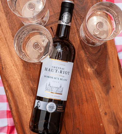 A Bottle of Sauvignon Blanc on a Wooden Board and Red and White Checkered Blanket with Wine Glasses.