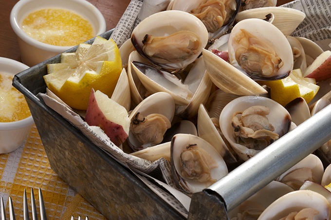 A catered clambake featuring fresh clams with potatoes, lemon wedges and butter.