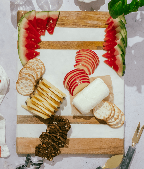 A Partially Assembled Charcuterie Board with Sliced Cheeses, A Whole Goat Cheese Log, Sliced Fruit, and Crackers.