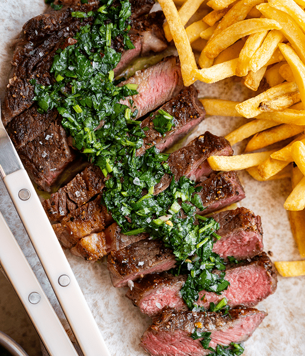 Sliced ribeye steak topped with chimichurri sauce and served with French fries.