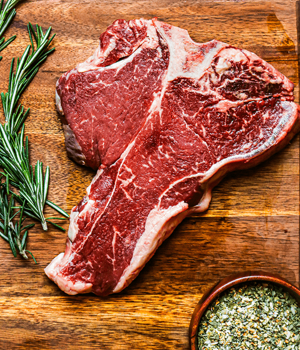 Heinen's Premium Raw Porterhouse Steak on a Cutting Board with a Sprig of Rosemary
