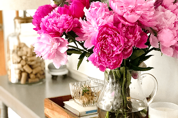 Table with a vase of open, pink peonies in water. 