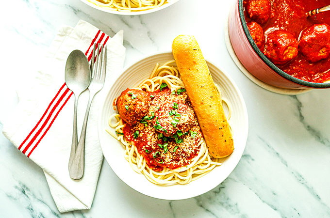Bowl of spaghetti with marinara, meatballs, and a garlic breadstick, next to a bowl of meatballs in sauce.