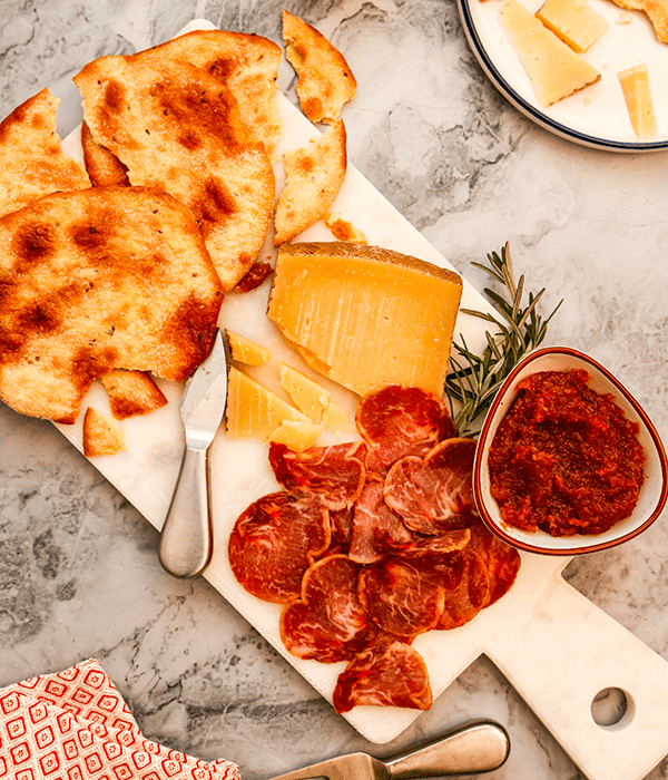 A Rectangular Stone Charcuterie Board with Sourdough Torta Crackers, a Block of Sliced Manchego Cheese, a Pile of Iberico Pork, and a Bowl of Membrillo Quince Paste 
