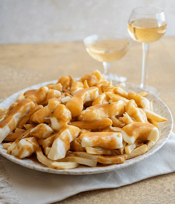 A Plate of Classic Poutine Beside two Wine Glasses Filled with White Wine