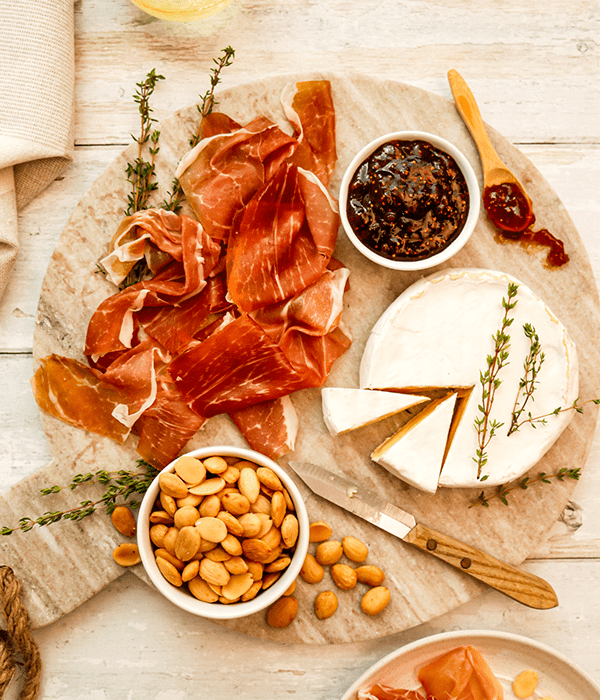A Charcuterie Board with Almonds, a Sliced Brie Cheese Wheel, a Bowl of Fig Spread, and a Pile of Prosciutto 