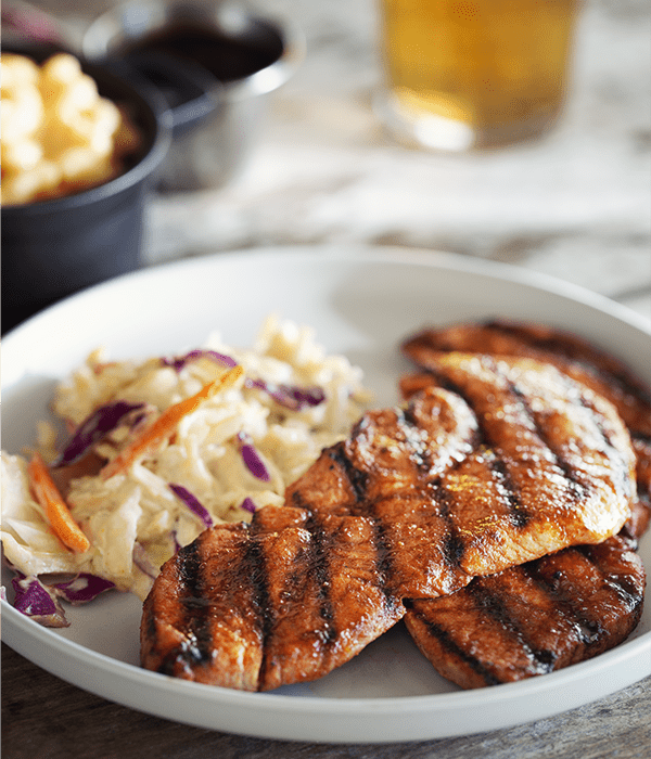 Whiskey Maple BBQ Pork Cutlets plated with a beverage and a side of mac n cheese.
