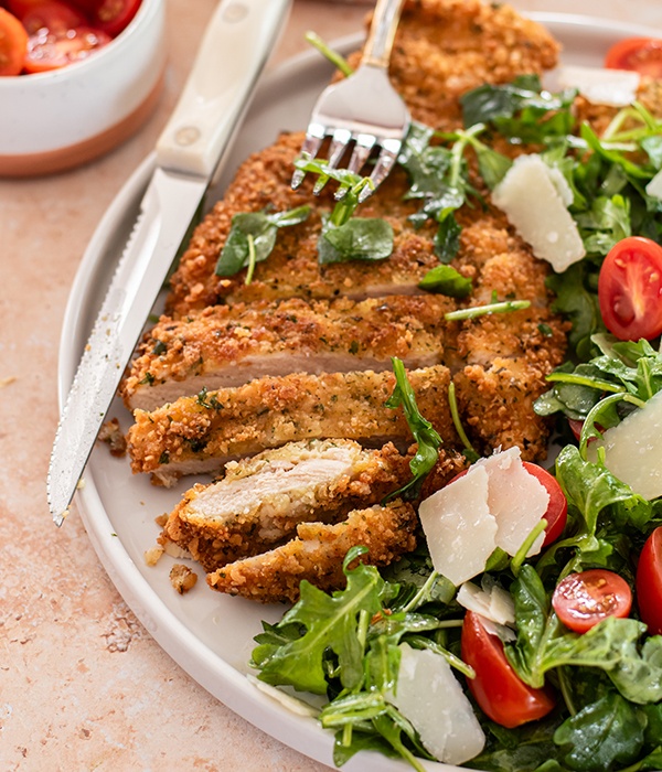 Crispy Chicken Milanese plated and sliced. Topped with arugula and bright cherry tomatoes.