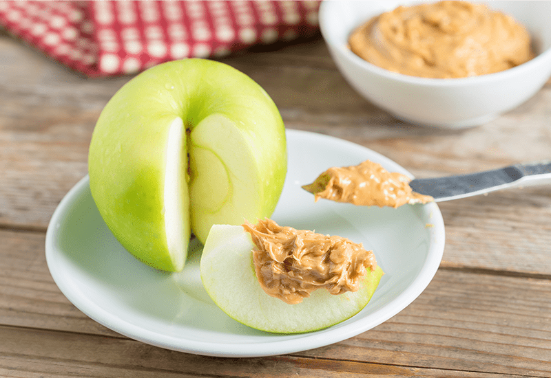 a Granny Smith Apple with Peanut butter on a plate with a knife