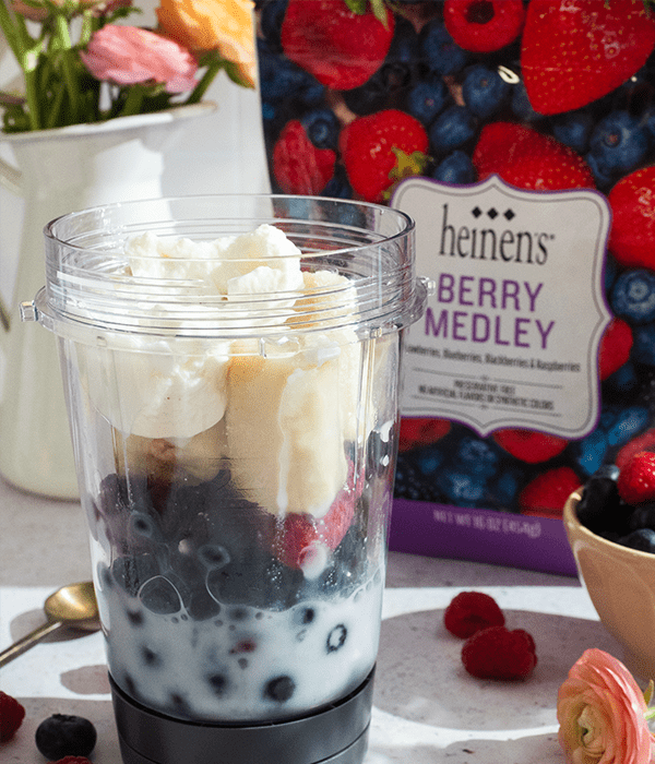 the Banana Berry Smoothie Bowl being blended together. Surrounded by a bag of the Heinen's fresh frozen fruit