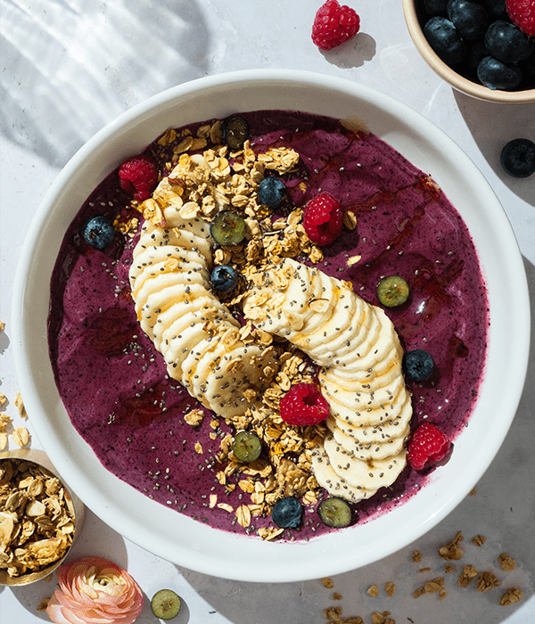 Banana Berry Smoothie Bowl plated next to some sides of fresh fruit and granola