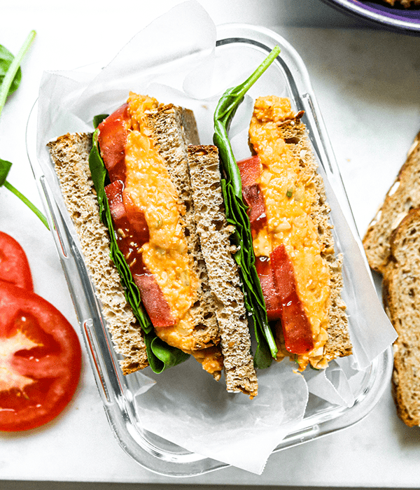 Buffalo Chickpea Salad Sandwich in a glass dish next to some extra bread and tomatoes