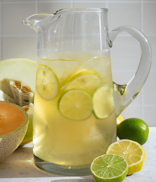 the Plum Wine Spritzer in a serving jug on a table surrounded by lemons and limes