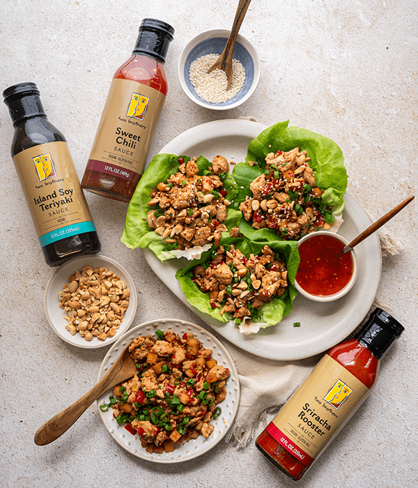 The Chicken Lettuce Wraps plated on a white plate surrounded by Two Brothers sauces and nuts